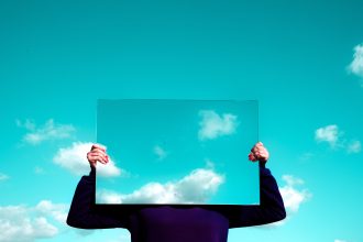 woman holding a mirror in front of her face, reflecting the sky and clouds