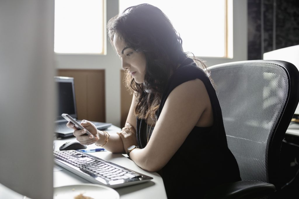 Woman using smart phone at office desk 