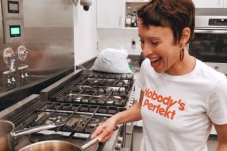 Emily Amarnick a Holistic Health Coach and Personal Chef smiling and cooking. Wearing a shirt that reads "nobody's perfect"