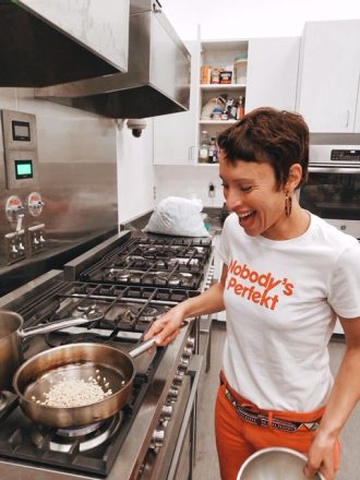Emily Amarnick a Holistic Health Coach and Personal Chef smiling and cooking. Wearing a shirt that reads "nobody's perfect"
