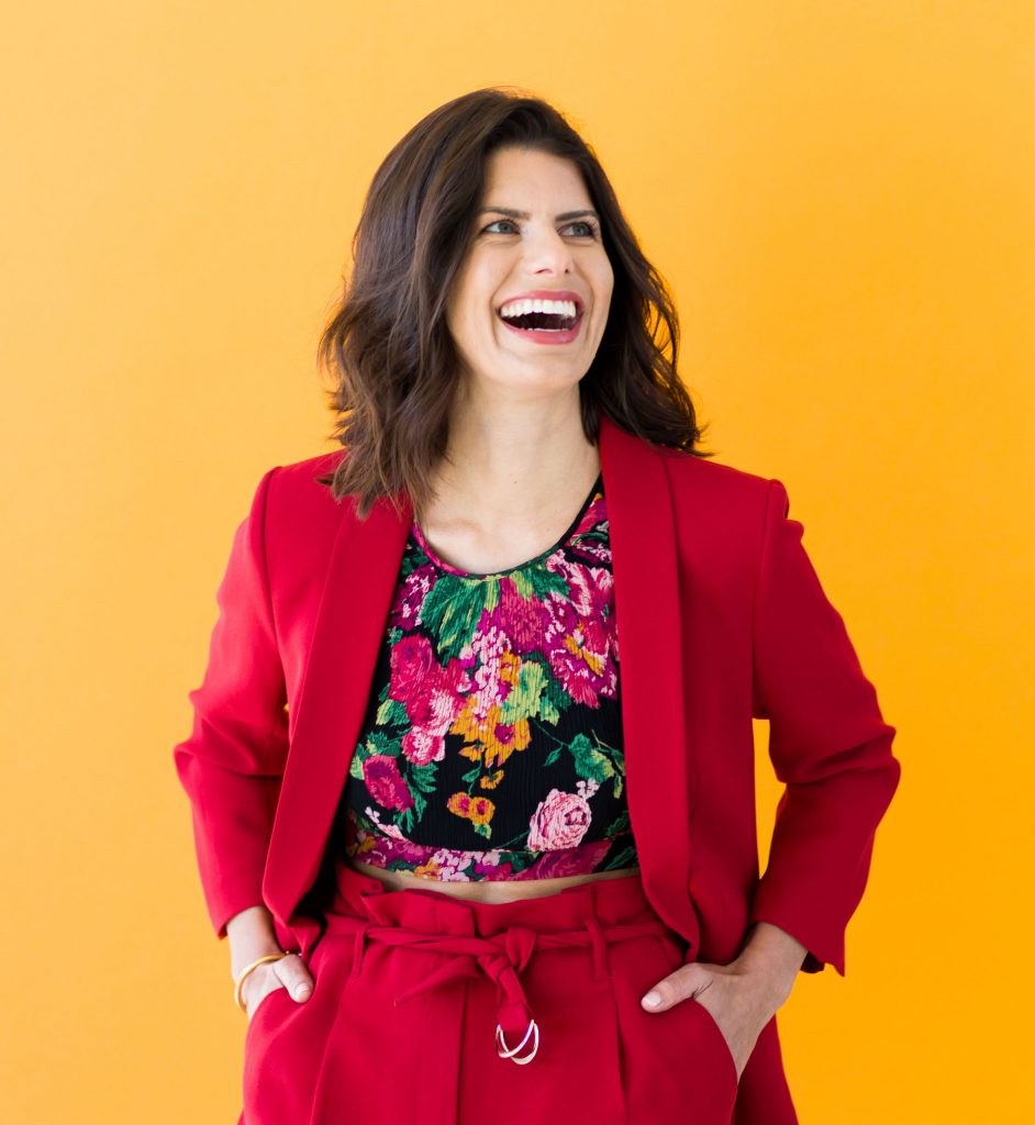 Margaux Joffe smiles wearing a red suit against a bright yellow background