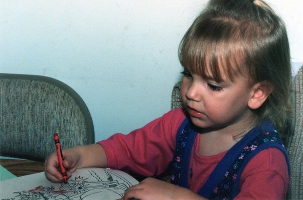 Dani as a young girl drawing with a red crayon