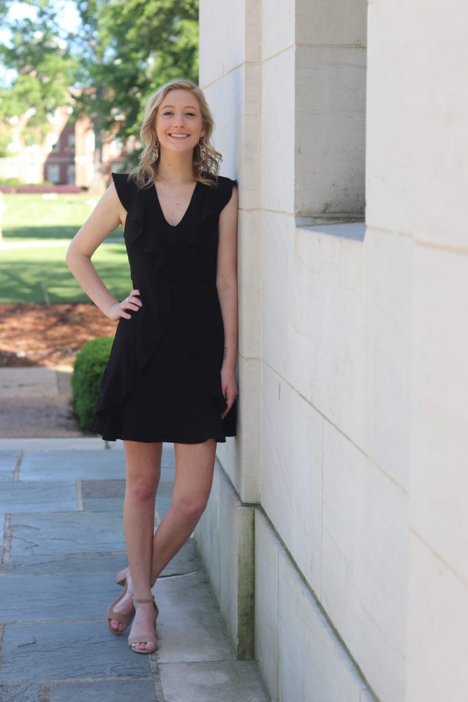 MacKenzie on campus, standing and smiling, wearing a black dress