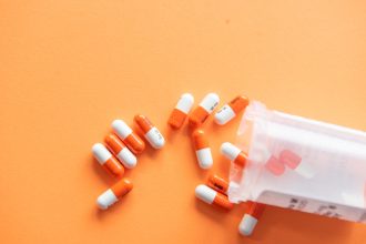 bottle of prescription pills against an orange backdrop