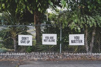 Signs on a chain link fence. Don't give up. You are not alone. You matter.