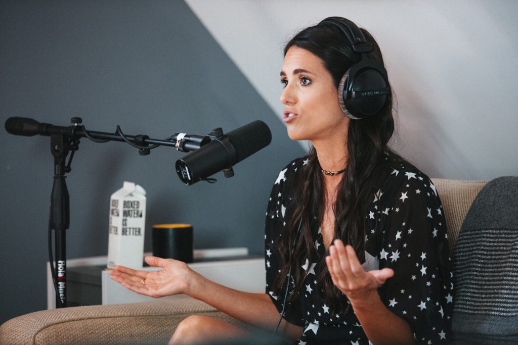 Liz speaking into a podcasting microphone, wearing headphones