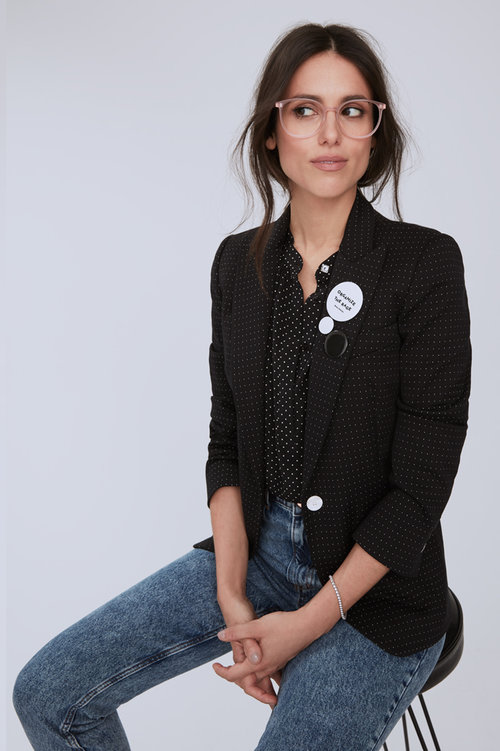 Liz Plank wearing a blazer and jeans on a stool
