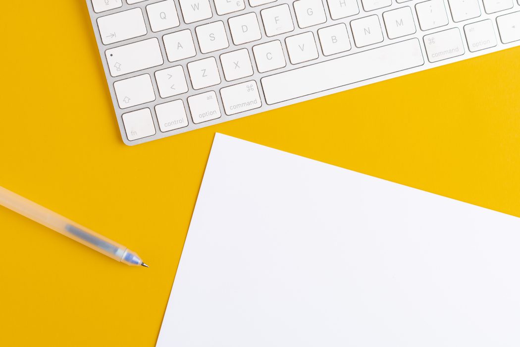 keyboard, blank sheet of paper and pen on a yellow desk