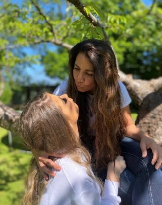 Dr Luiza Sanz and her daughter blow each other air kisses in front of a beautiful green tree