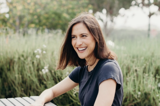 Emily smiling sitting at a picnic table in a lush meadow.