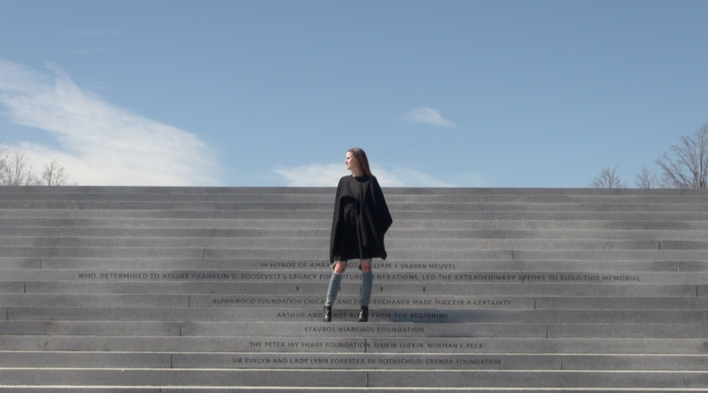 Woman standing on steps made of rock. She is wearing ripped jeans and black coat.